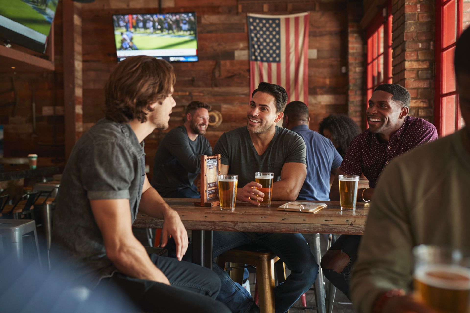 group of male friends drinking beer at a bar watching sports